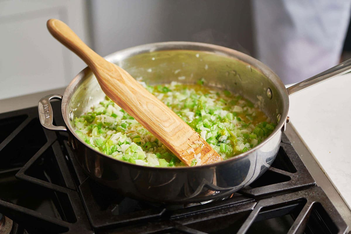 Wooden spatula in a skillet with sauteing onions and celery.