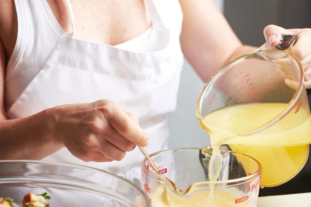 Woman pouring broth into a measuring cup with eggs.