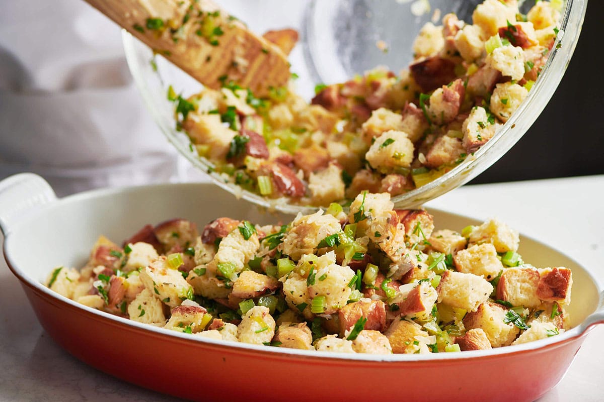 Stuffing mixture pouring into a red baking dish.