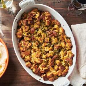 Classic stuffing on Thanksgiving dinner table with bowls of mashed potatoes.