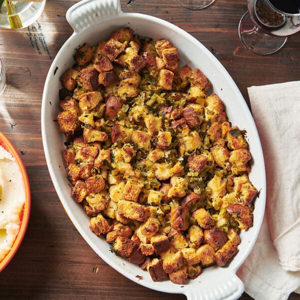 Classic stuffing on Thanksgiving dinner table with bowls of mashed potatoes.
