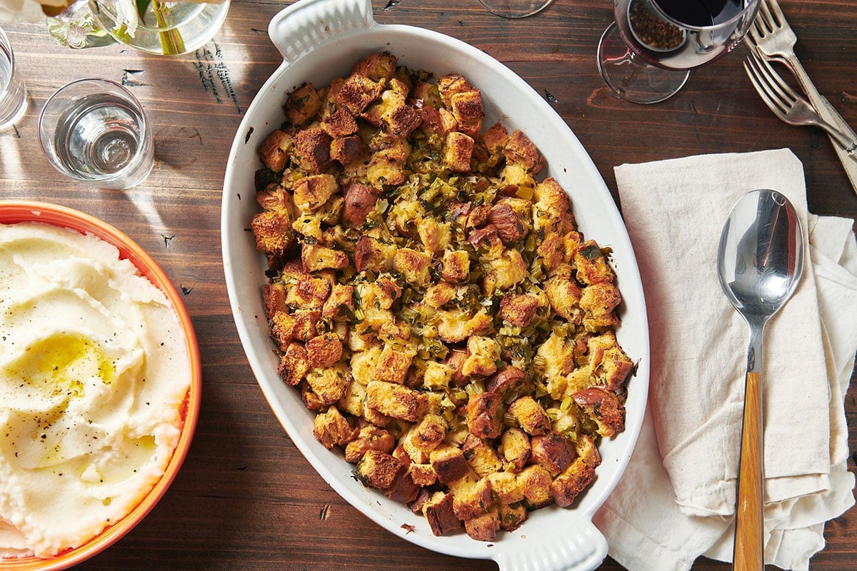 Classic stuffing on Thanksgiving dinner table with bowls of mashed potatoes.