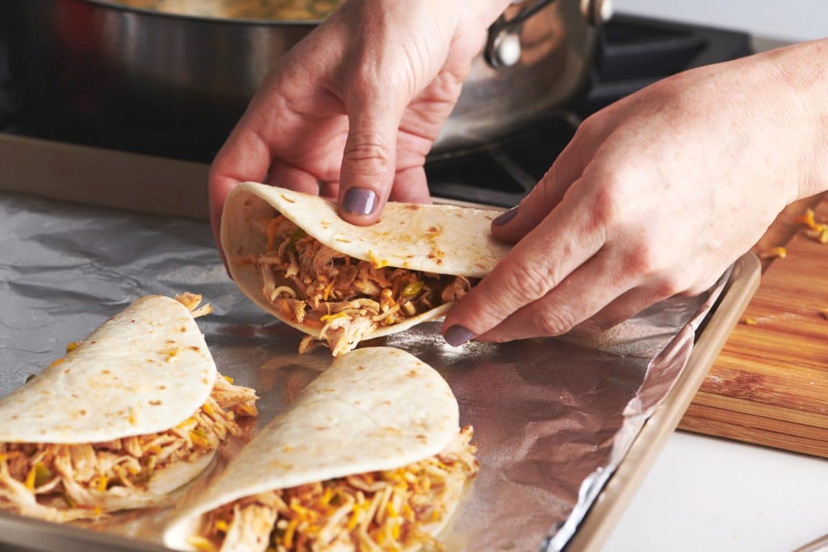 Woman placing folded tortillas filled with chicken on a foil-lined baking sheet.