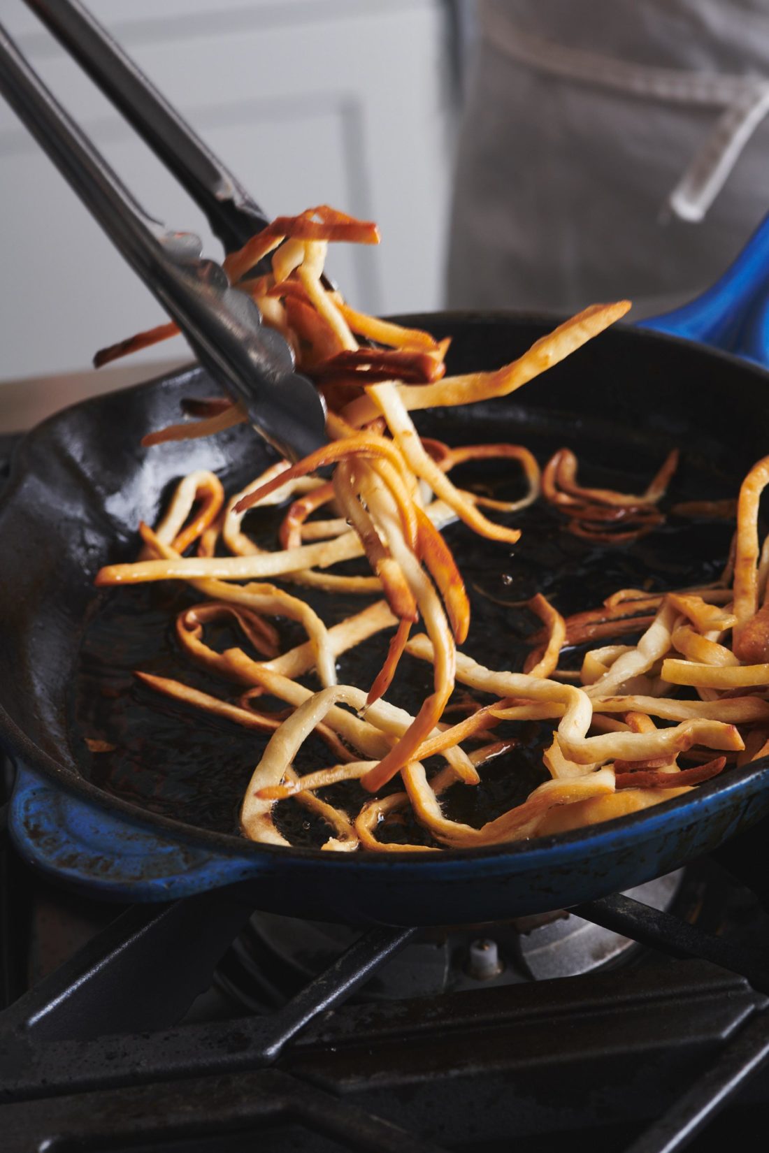 Tongs tossing tortilla strips in a skillet.