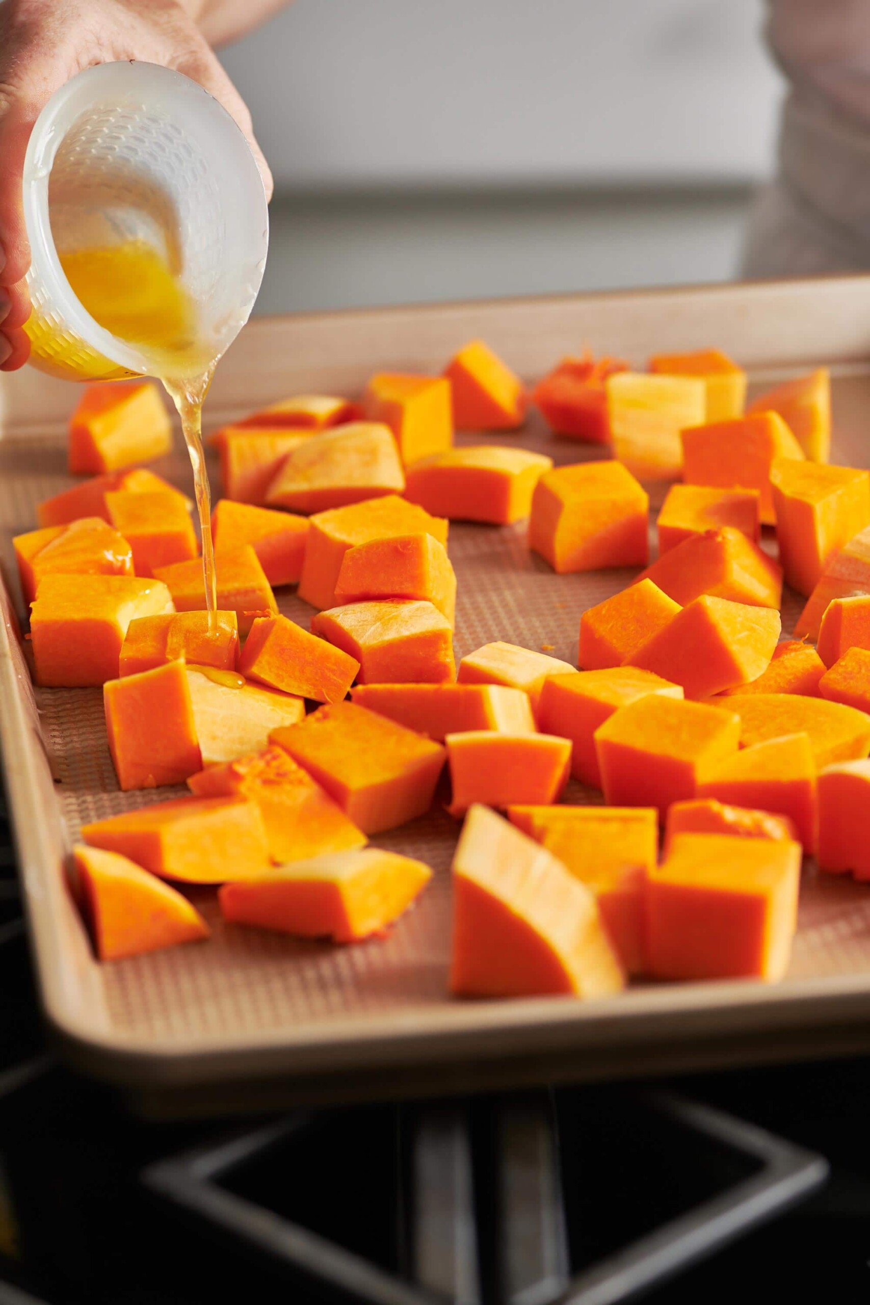 Woman pouring melted butter over cubes of Butternut Squash.