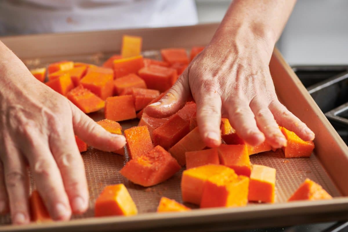 Woman mixing cubes of Butternut Squash with brown sugar and salt with her hands.