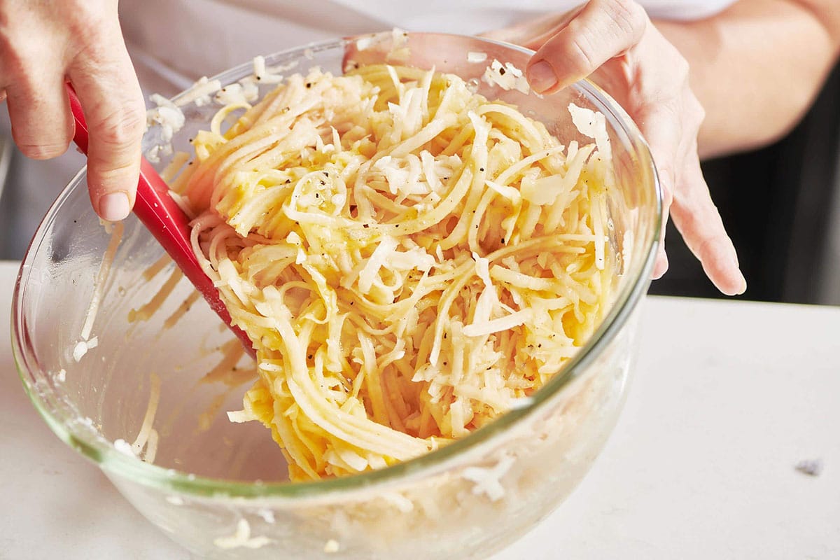 Woman stirring potato pancake mixture in glass bowl.