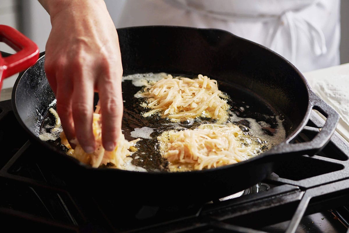 Woman placing potato pancakes mixture into a hot cast iron skillet
