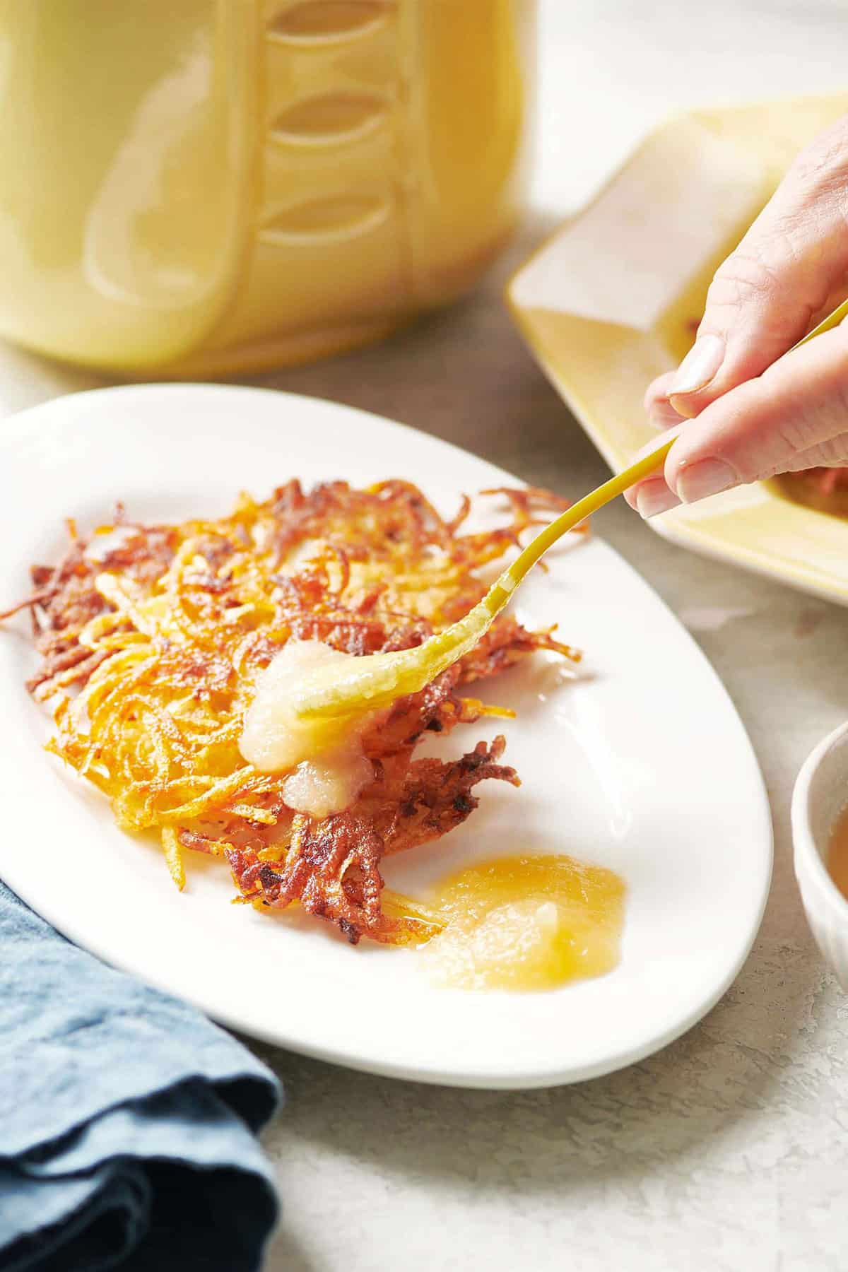 Spoon adding applesauce to a latke on a plate.