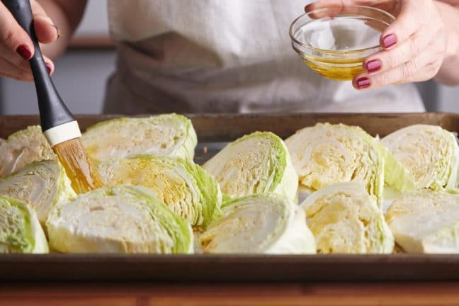 Woman brushing oil onto cabbage wedges on a baking sheet.