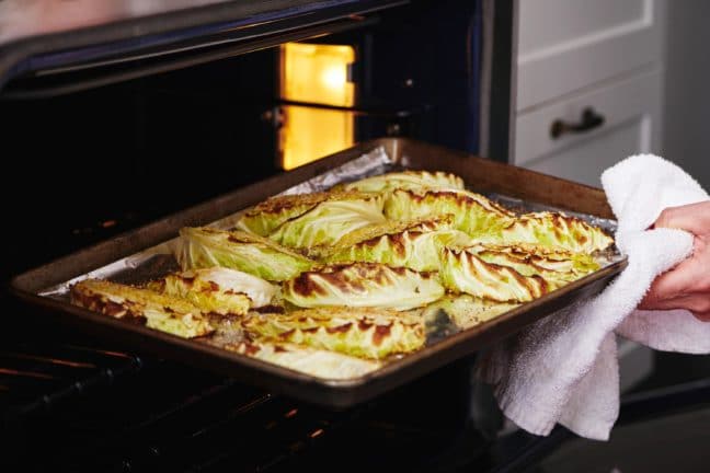 Woman removing a tray of Roasted Cabbage Wedges from the oven.