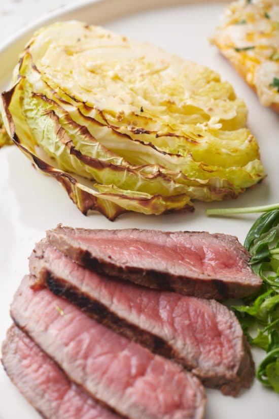 Roasted Cabbage Wedge on a plate with meat and greens.