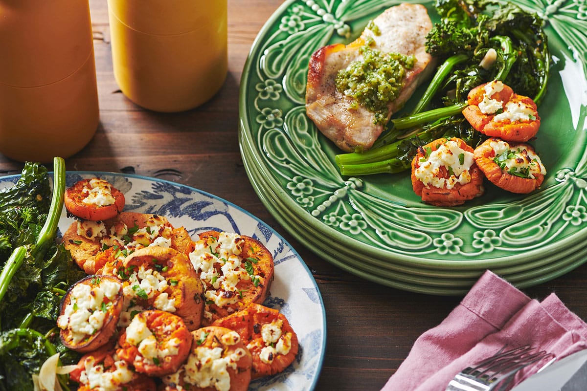 Smashed Garlic Butter Sweet Potatoes with Feta on plates with pork and vegetable side.