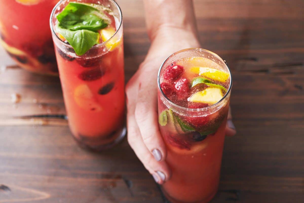 Woman grabbing one of two glasses of Fruit and Berry Sangria on a table.