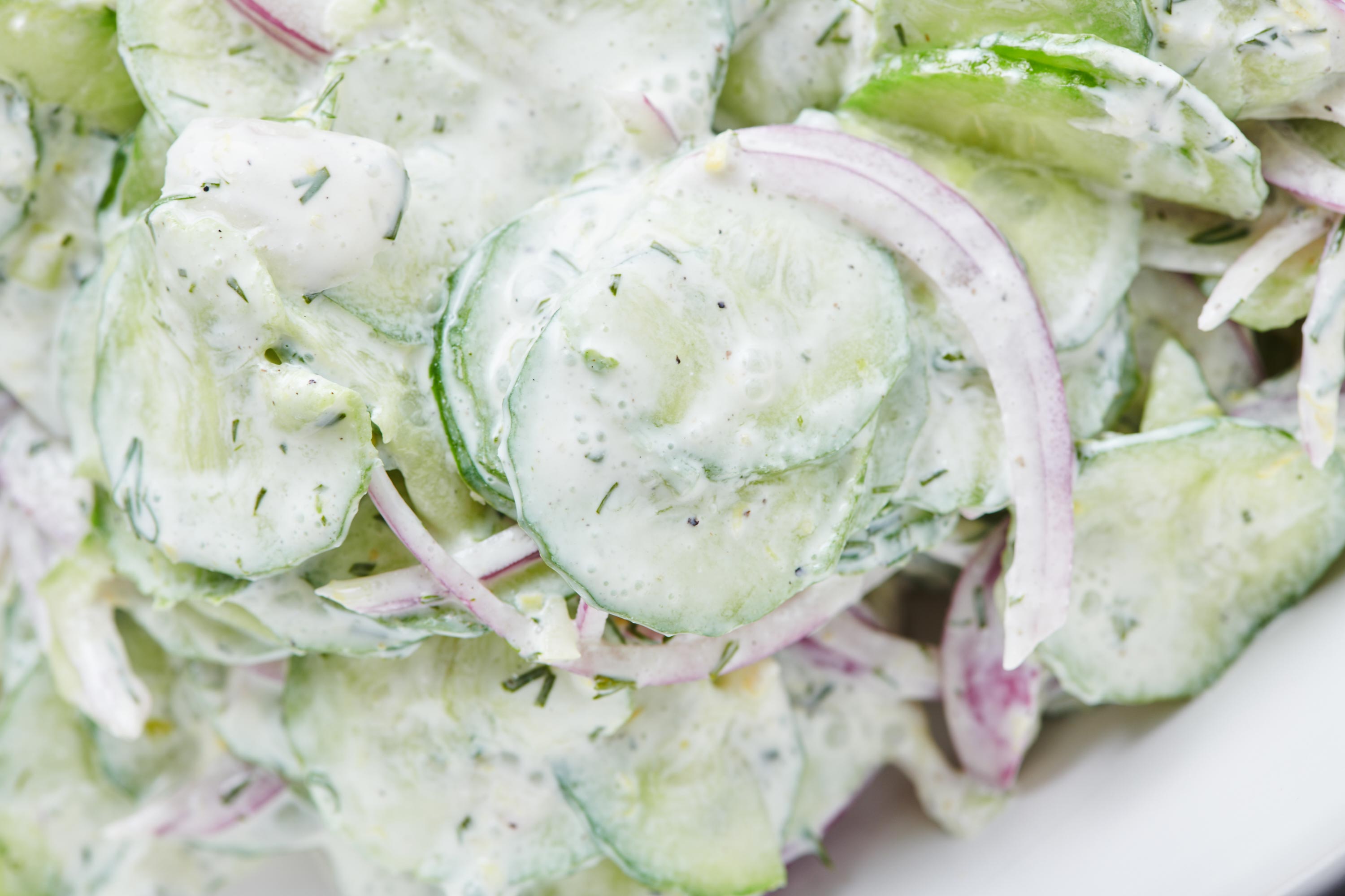 Pile of cucumber salad with a creamy sour cream dressing and red onion and dill.