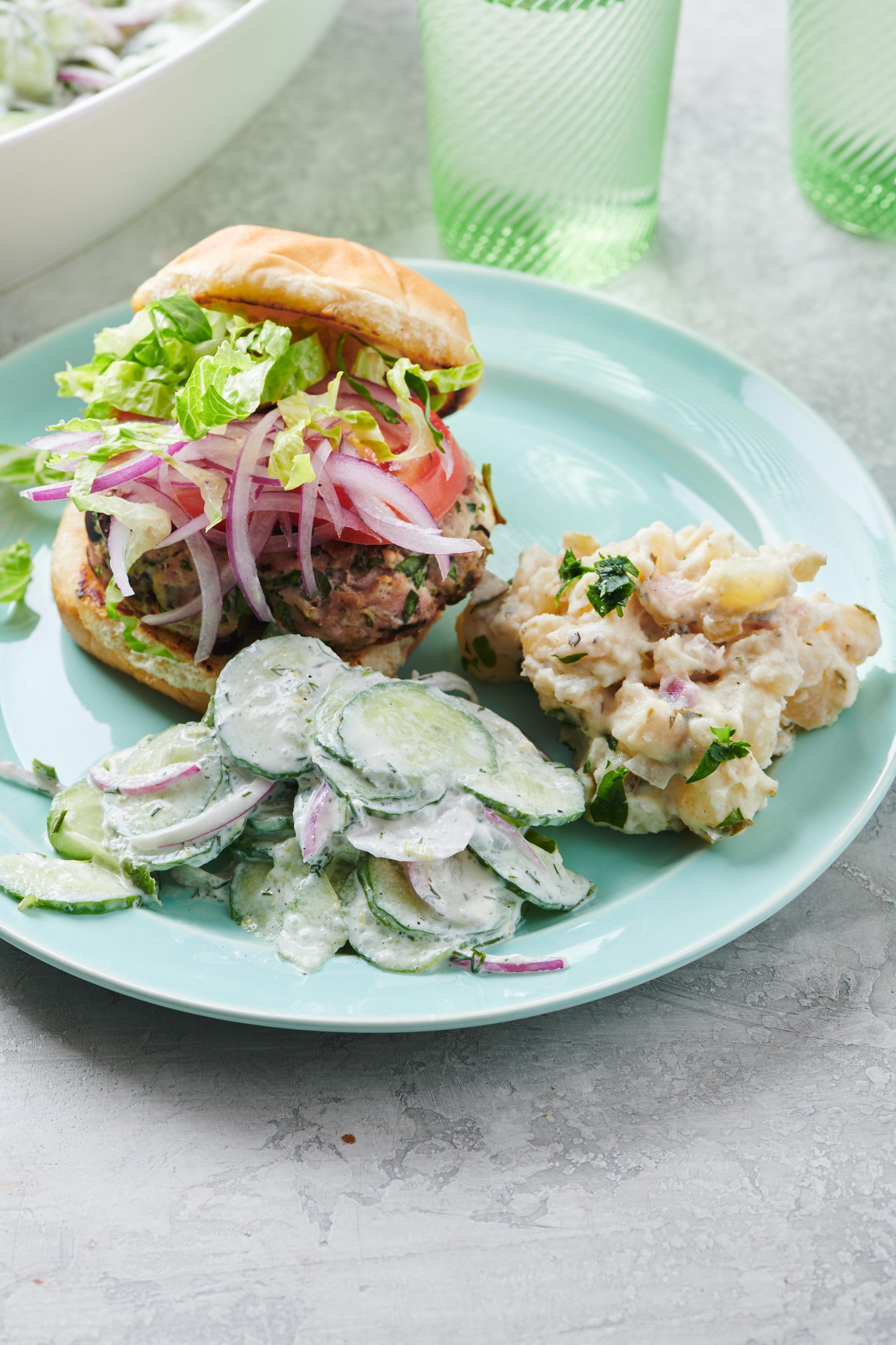 Creamy Cucumber Salad on an aqua blue plate with a Greek turkey burger and a scoop of potato salad.