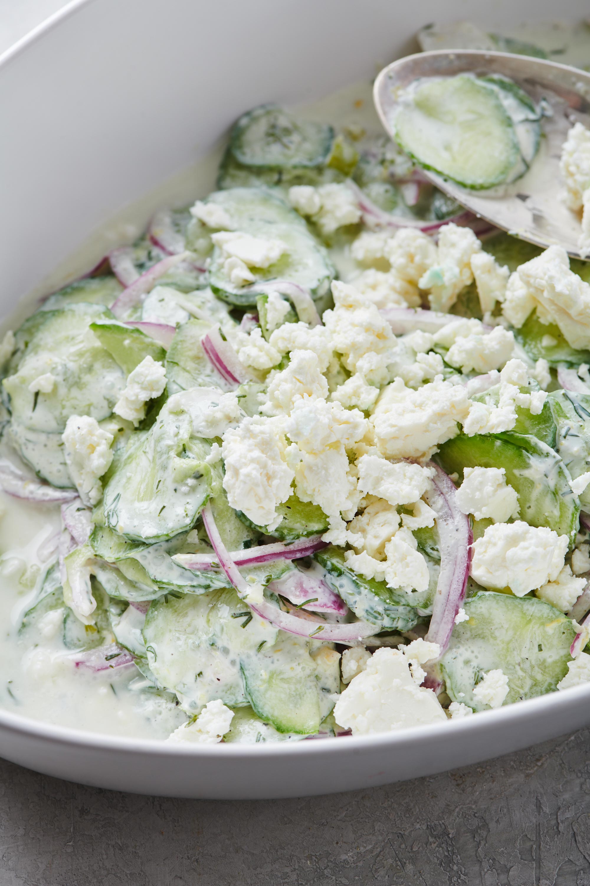 Cucumber Salad with a creamy dressing with  crumbled goat cheese on top in a white bowl.