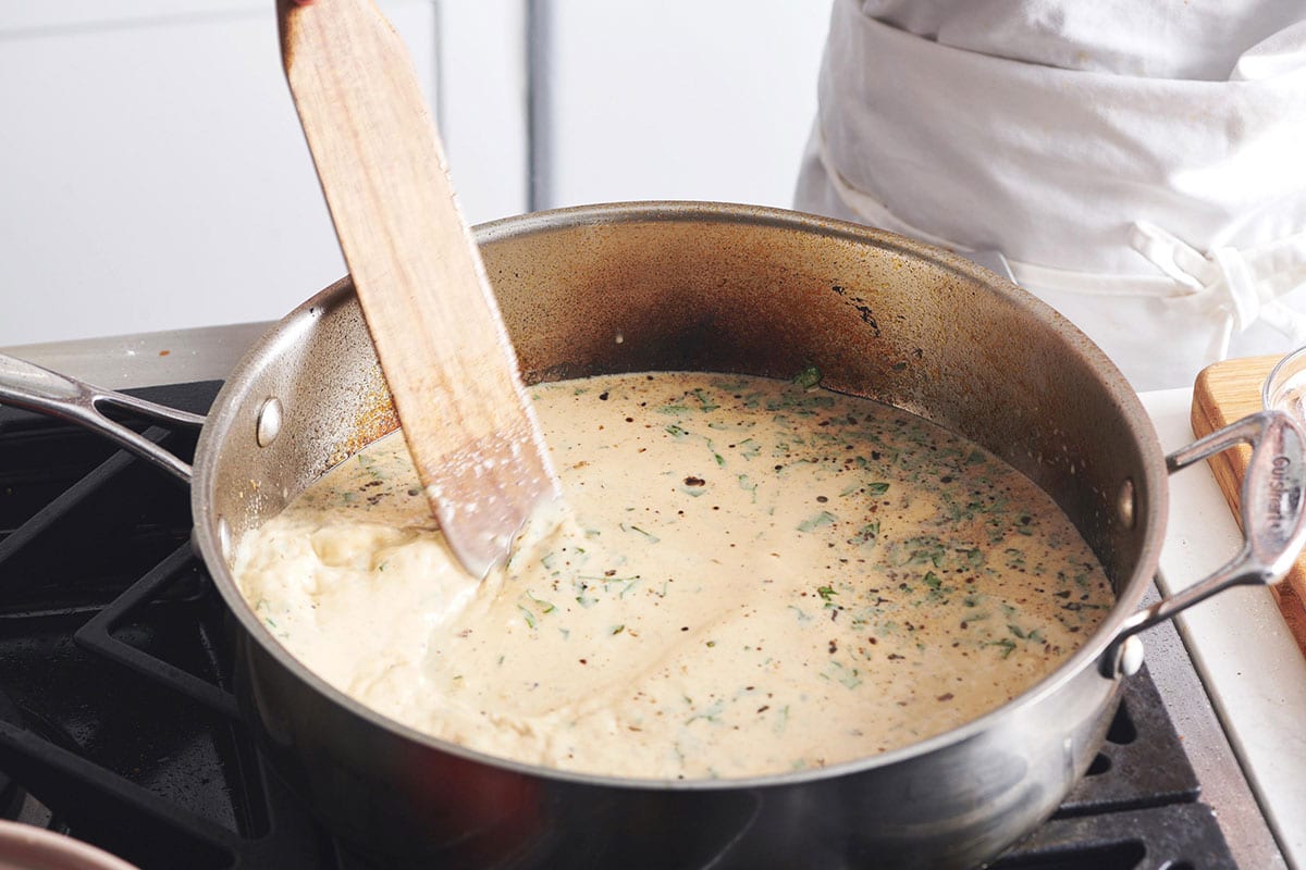 Stirring cream sauce in pan on stove.