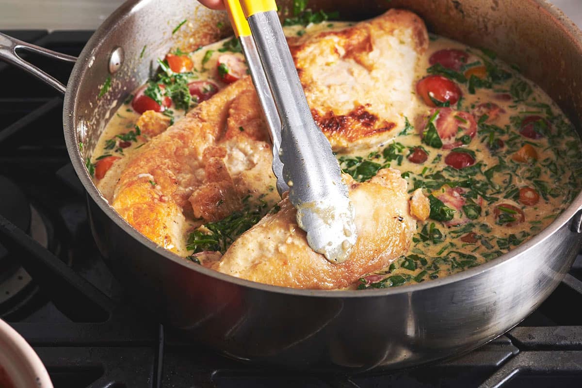 Stirring chicken in pan of Tuscan sauce.