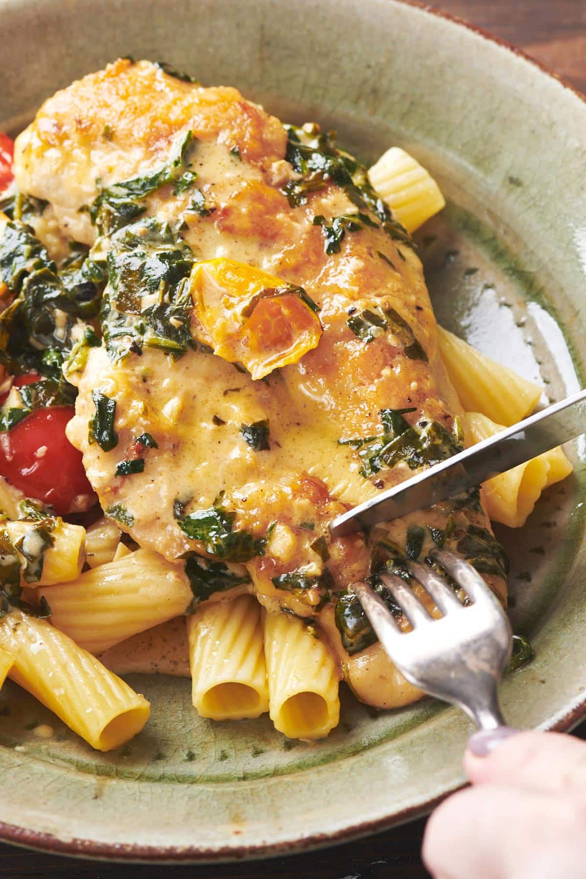 Fork cutting Creamy Tuscan Chicken with Pasta on green plate.