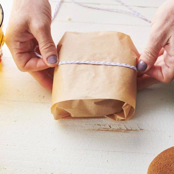 Woman tying twine around Gingersnaps in parchment paper.