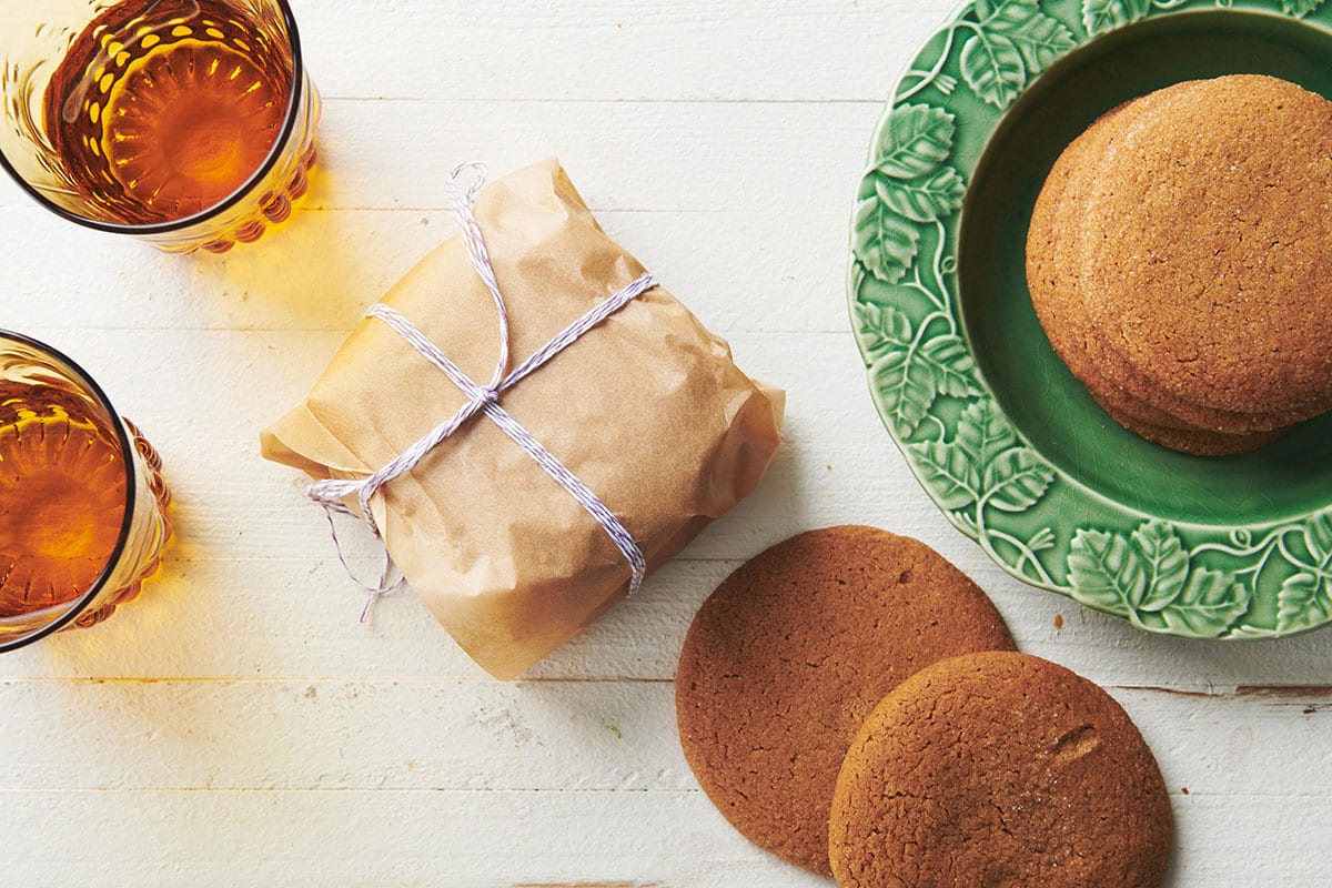Table with gingersnaps on green plate and wrapped in parchment next to drinks.