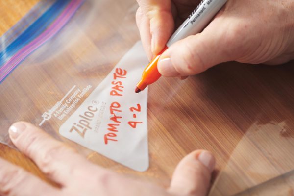 Woman using a sharpie to label a Ziploc bag \"Tomato Paste.\"
