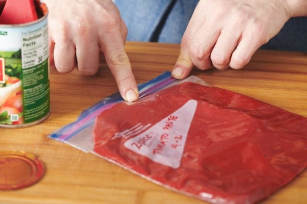 Woman sealing a Ziploc bag of tomato paste.