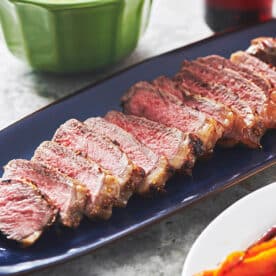 Sliced Pepper-Mustard Strip Steaks on blue serving tray.