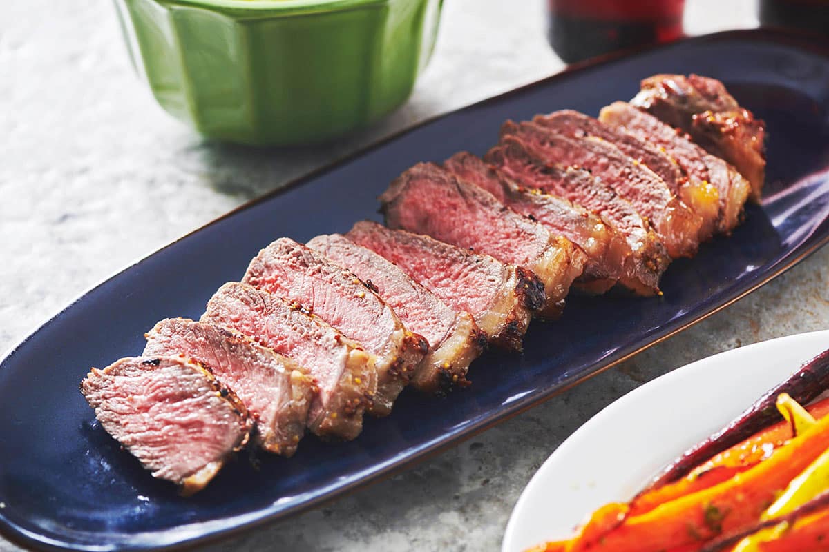Sliced Pepper-Mustard Strip Steaks on blue serving tray.