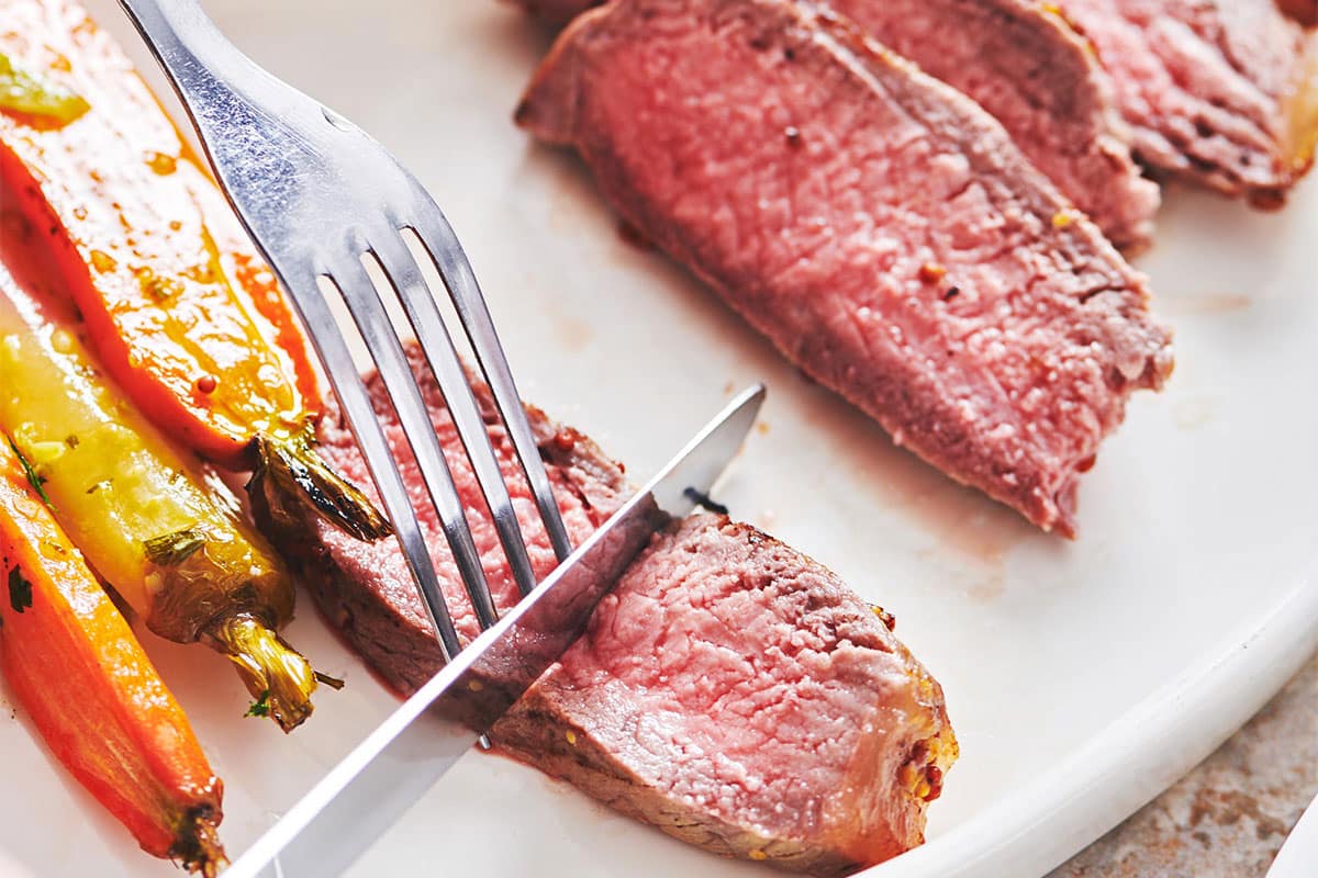 Slicing strip steak with knife on plate.