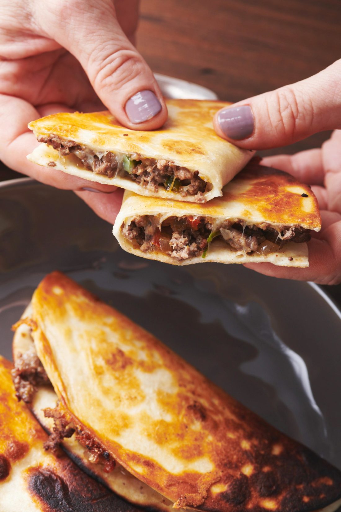 Woman holding two Cheesy Ground Beef and Vegetable Quesadillas.