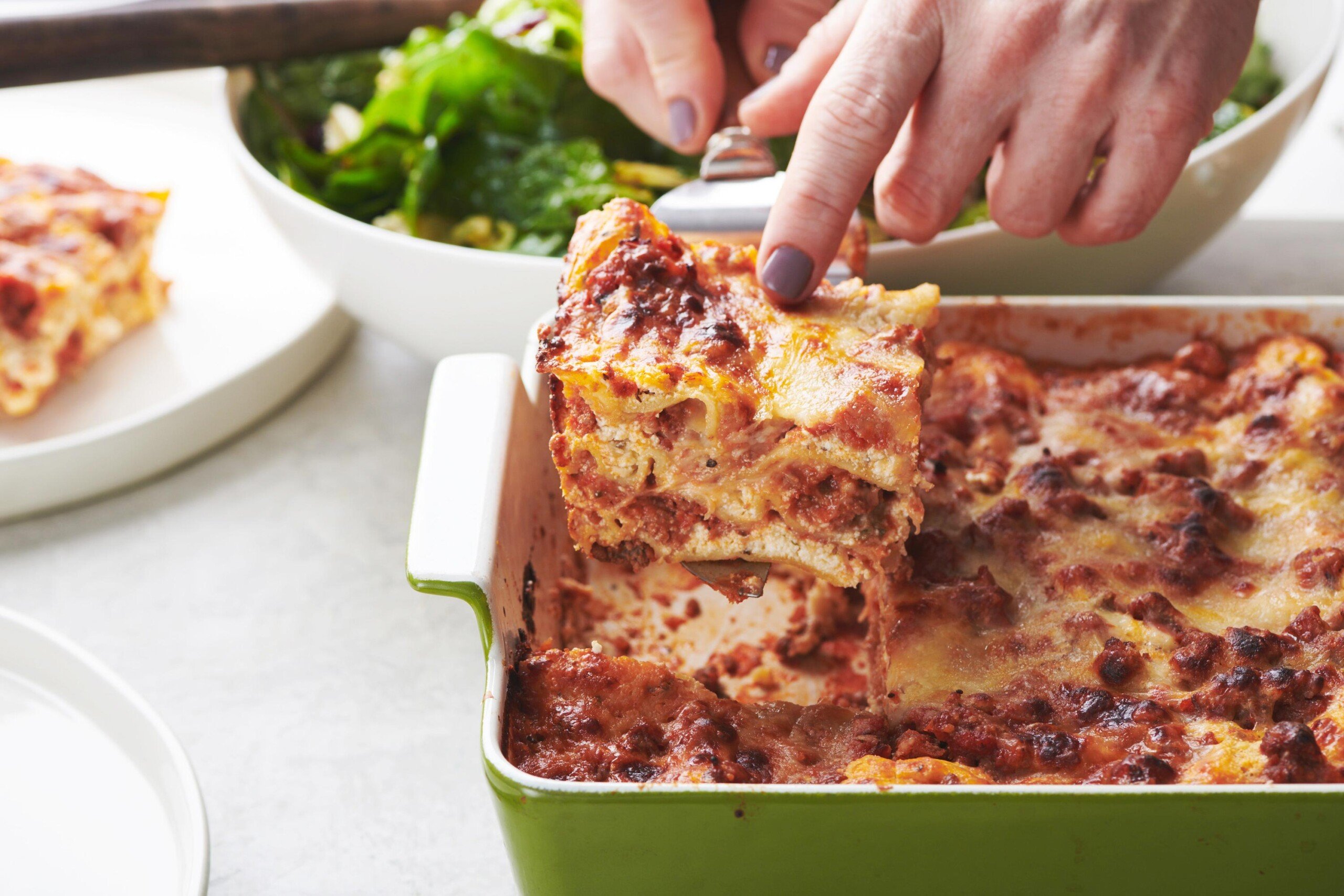 Woman using a spatula to grab a slice of Lasagna.