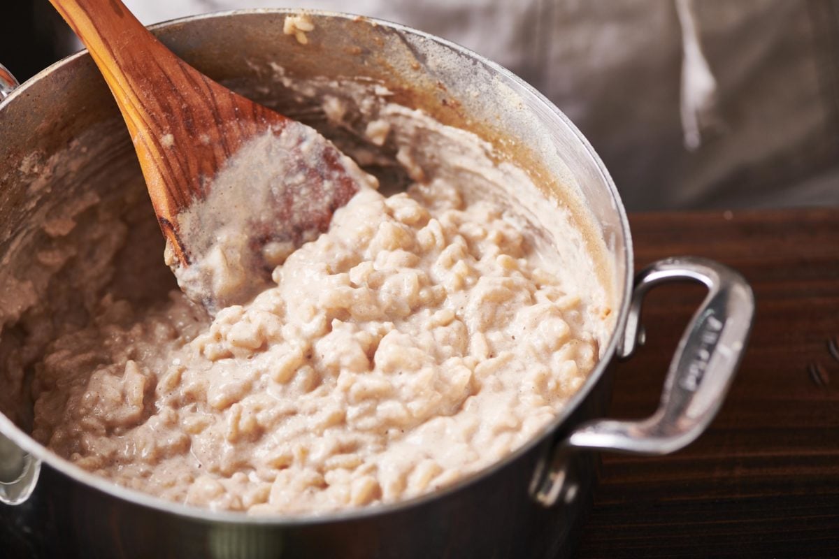 Wooden spoon stirring a pan of Creamy Rice Pudding.