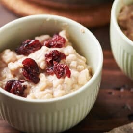 Rice pudding topped with dried cranberries in small bowl on table.