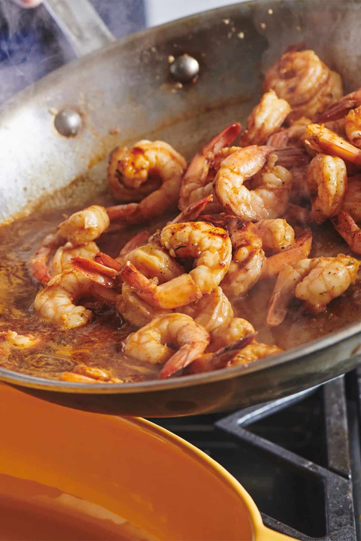 Pouring Creole Shrimp from pan into yellow dish.