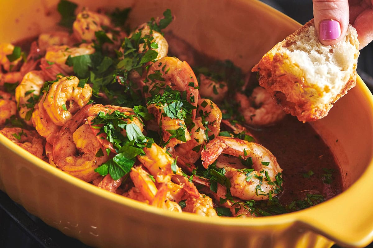 Woman dipping bread into a bowl with Creole Shrimp.