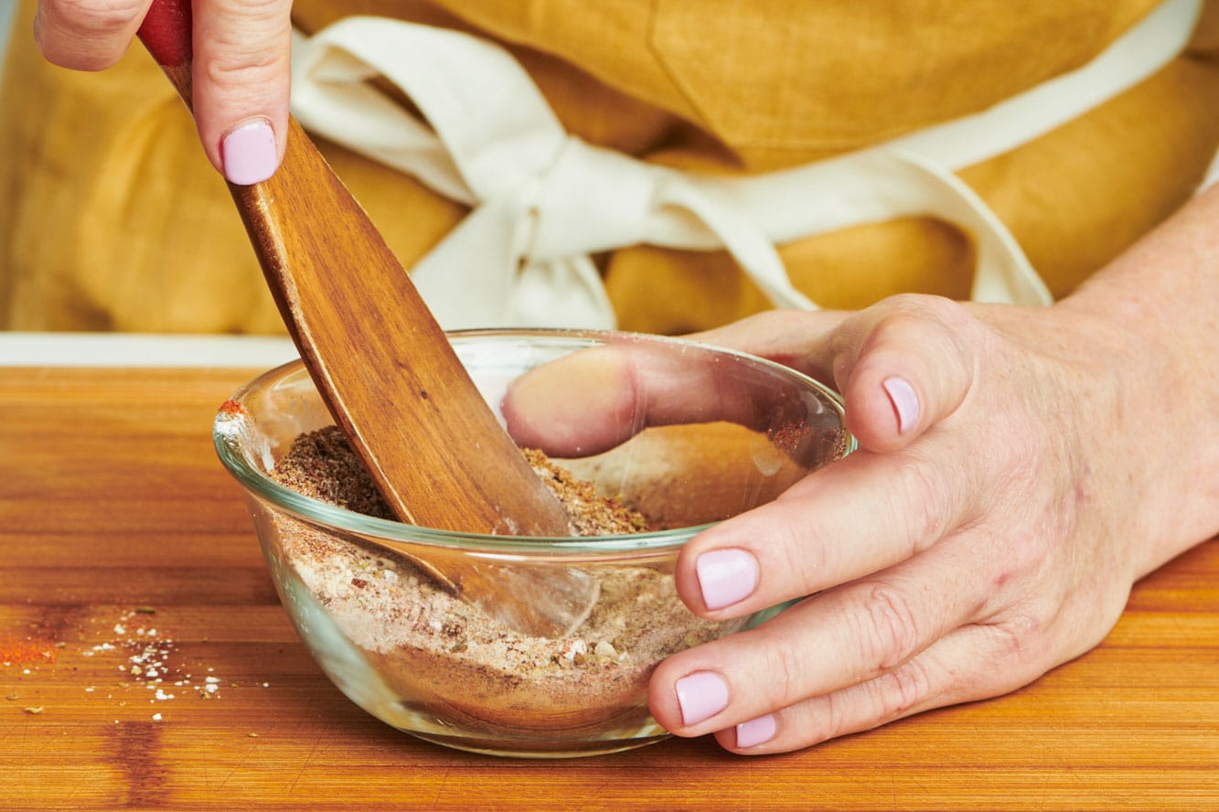 Mixing spices in small bowl with wood spoon.