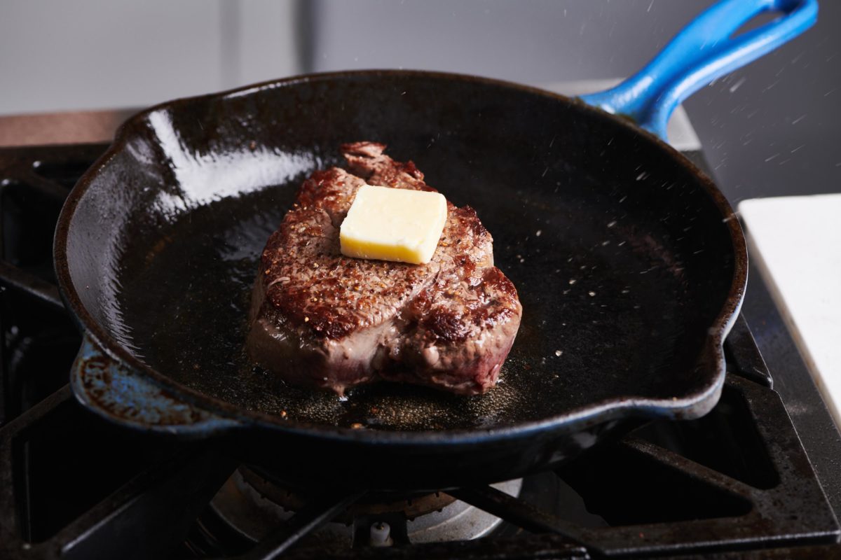 Filet Mignon in a skillet topped with a pat of butter.