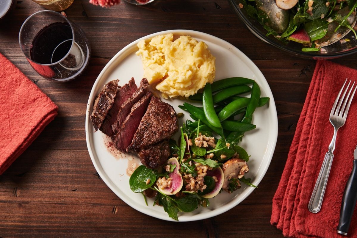 Salad, mashed potatoes, vegetables, and filet mignon on a white plate.