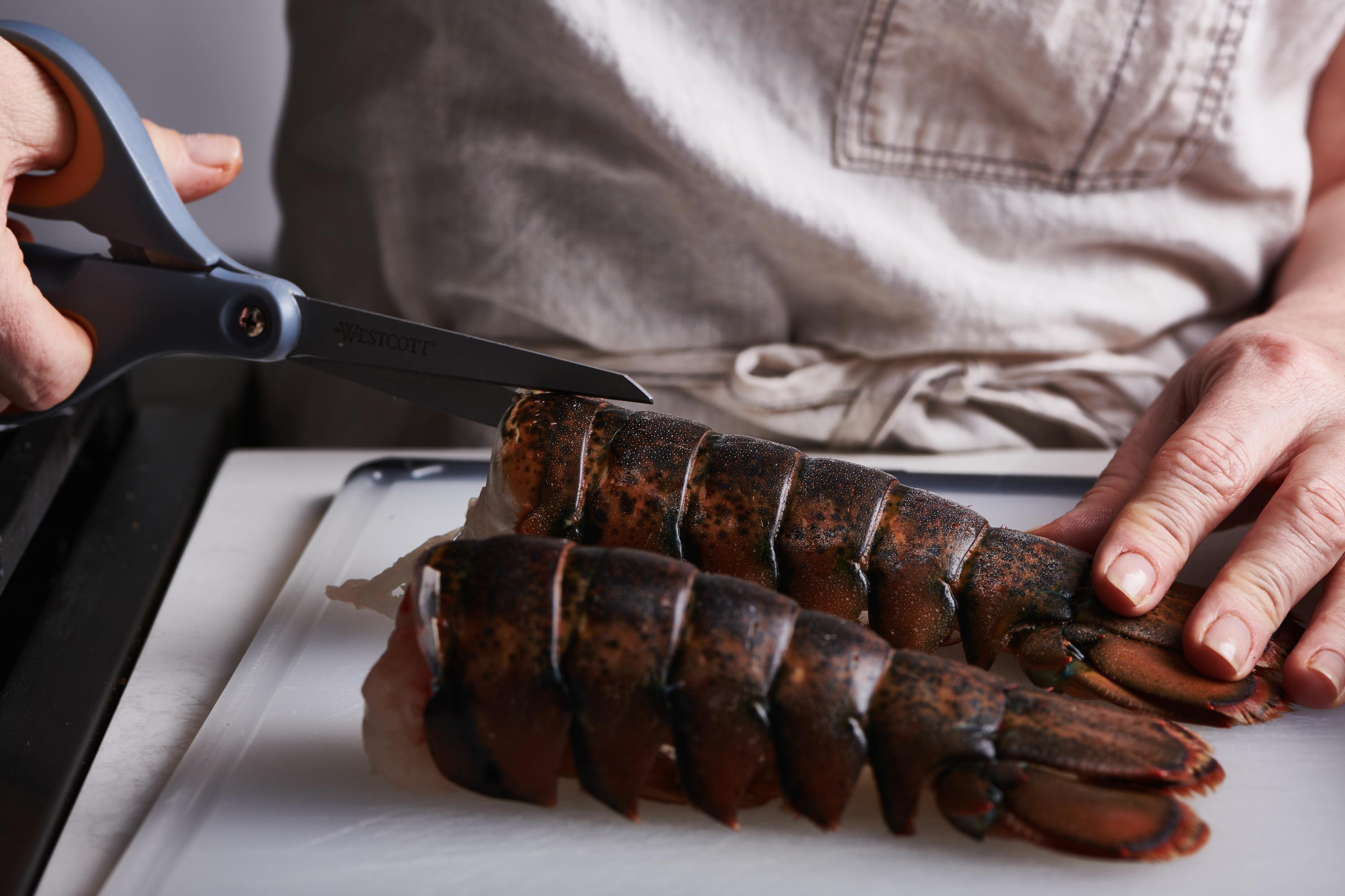 Woman cutting lobster tail shells on a cutting board.