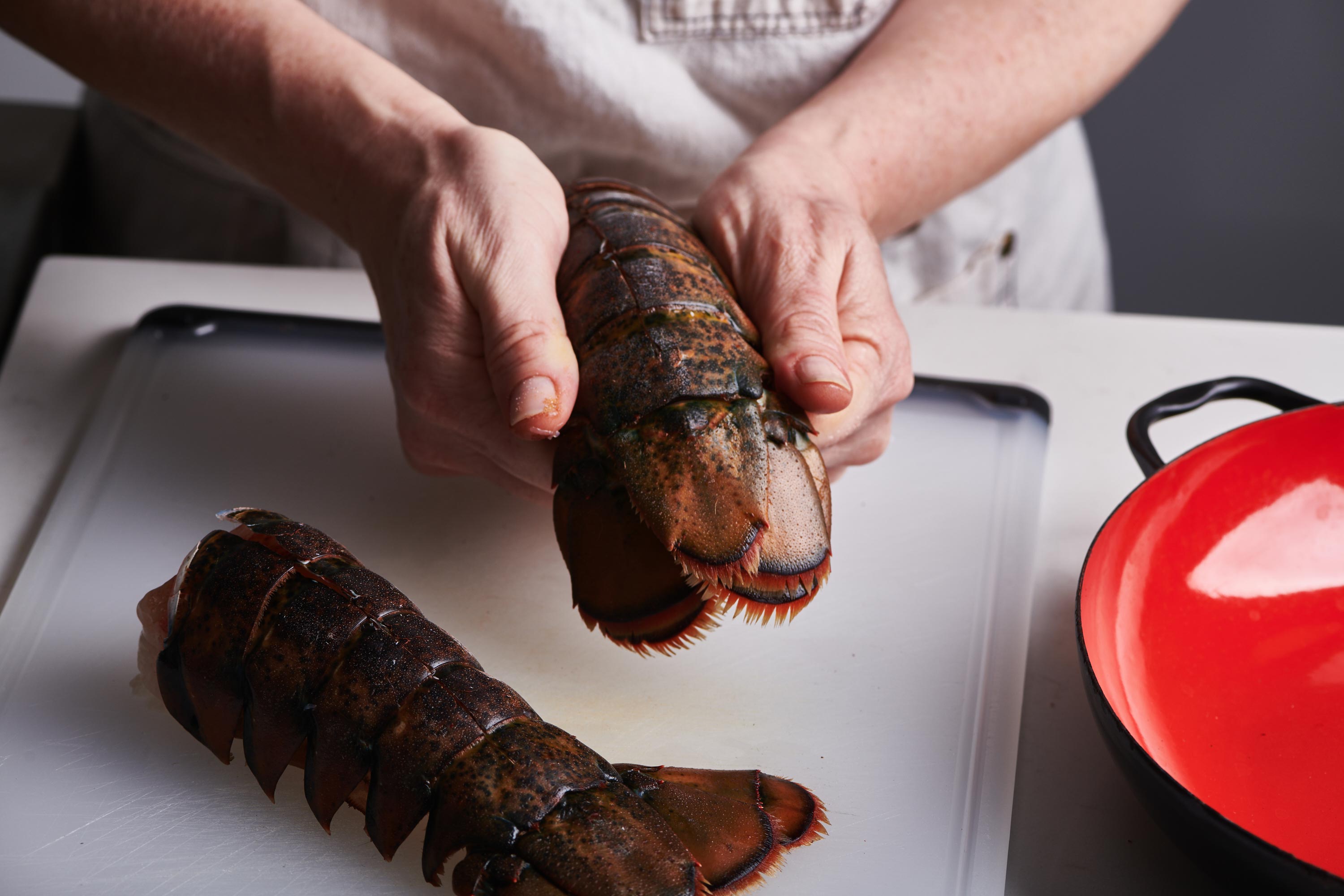 Woman holding a lobster tail with another lobster tail on a cutting board.