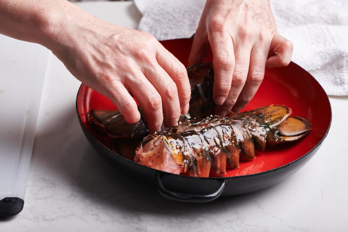 Woman placing lobster tails in red pan.