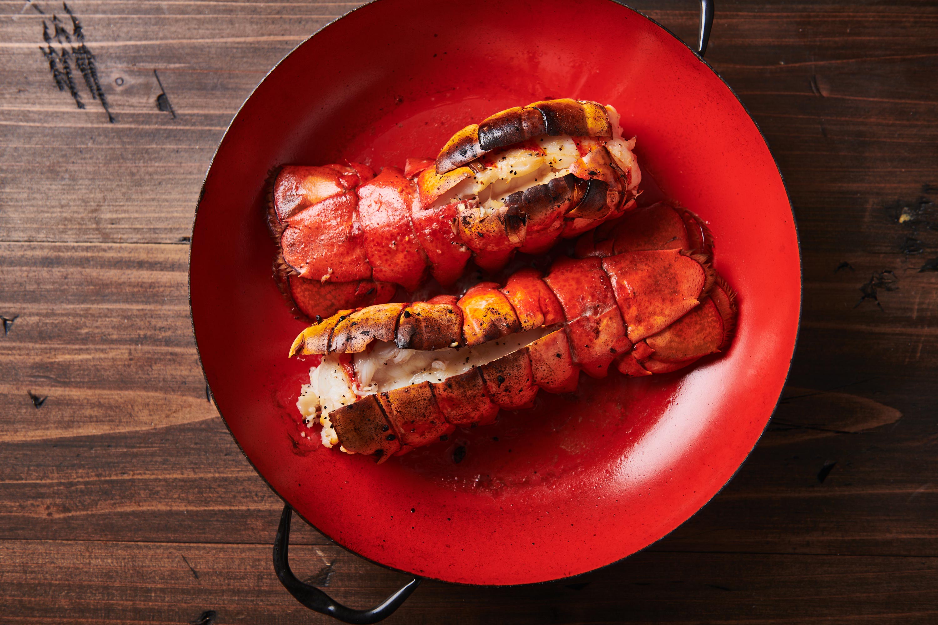 Two broiled lobster tails on a red baking pan.