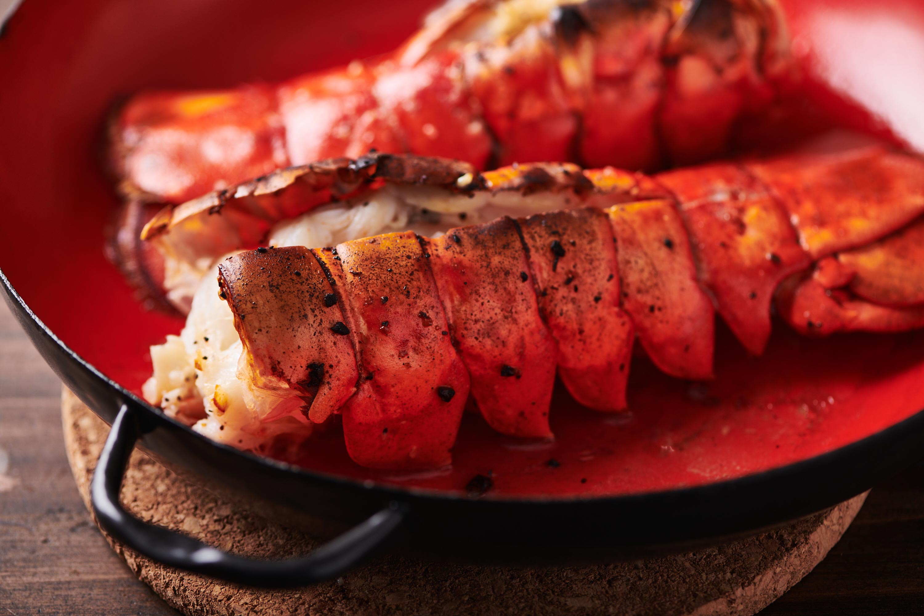 Two split broiled lobster tails in a red baking dish.