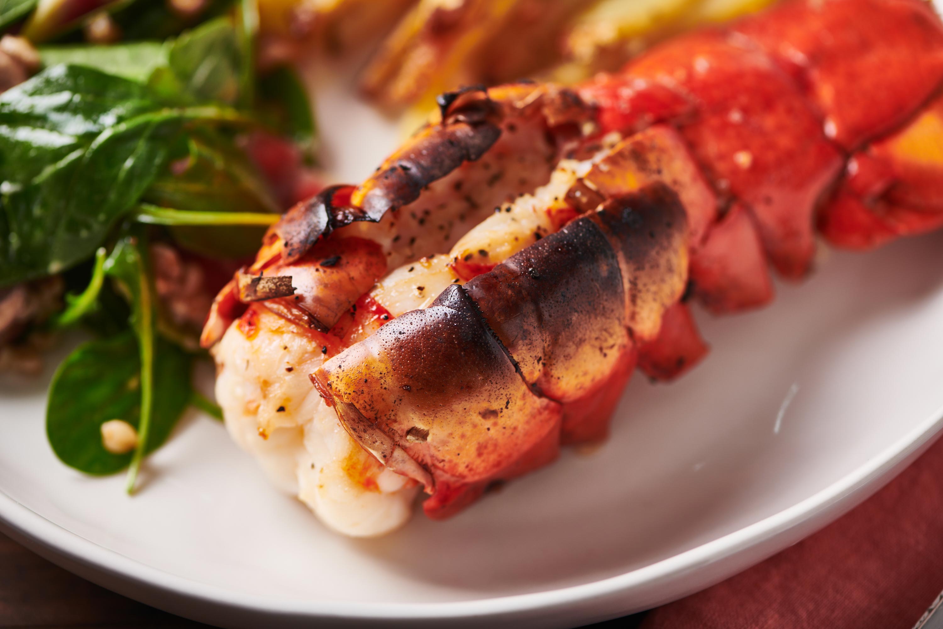 Split broiled lobster tail on a plate with salad.