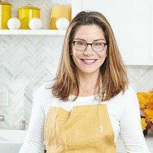 Katie Workman with apron in kitchen at cutting board.