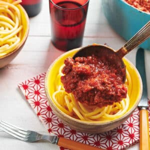 Pouring homemade Italian meat sauce over bowl of spaghettie.