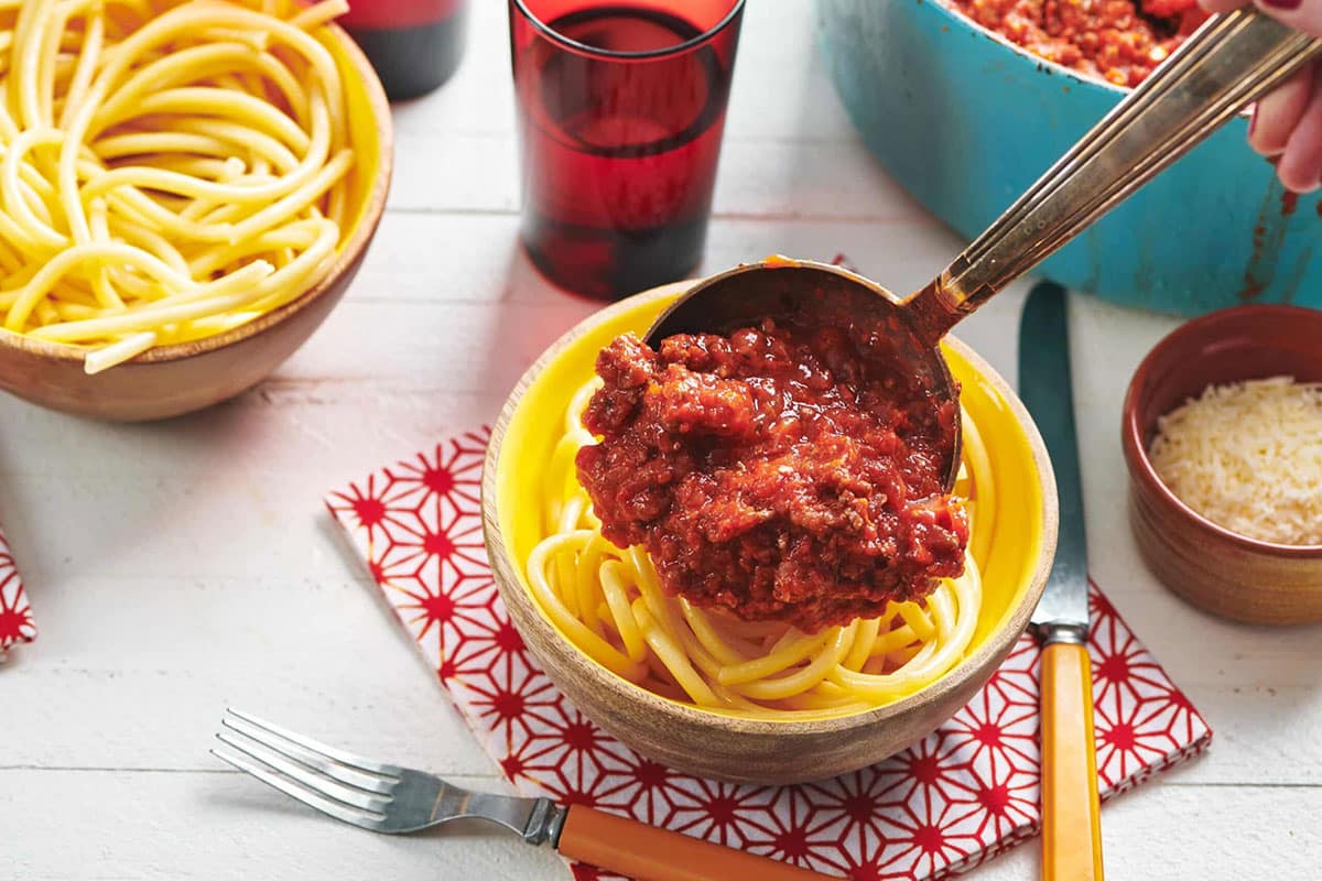 Pouring homemade Italian meat sauce over bowl of spaghettie.