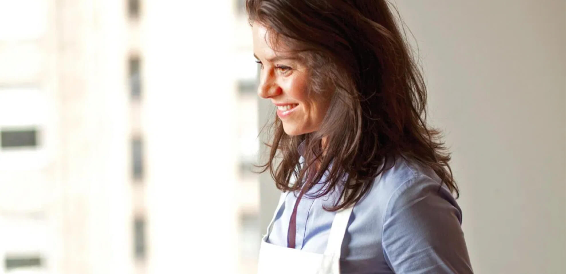 Katie Workman smiling and wearing a blue shirt and a white apron.